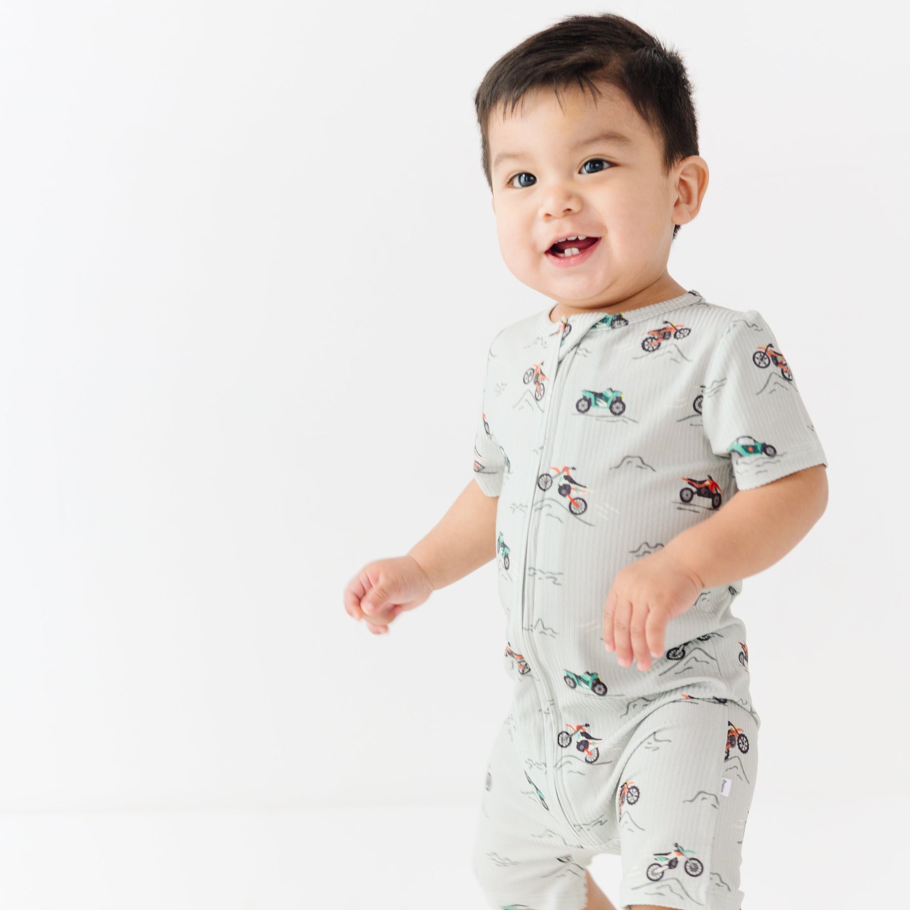 Baby wearing a light gray onesie with vehicle patterns on a white background