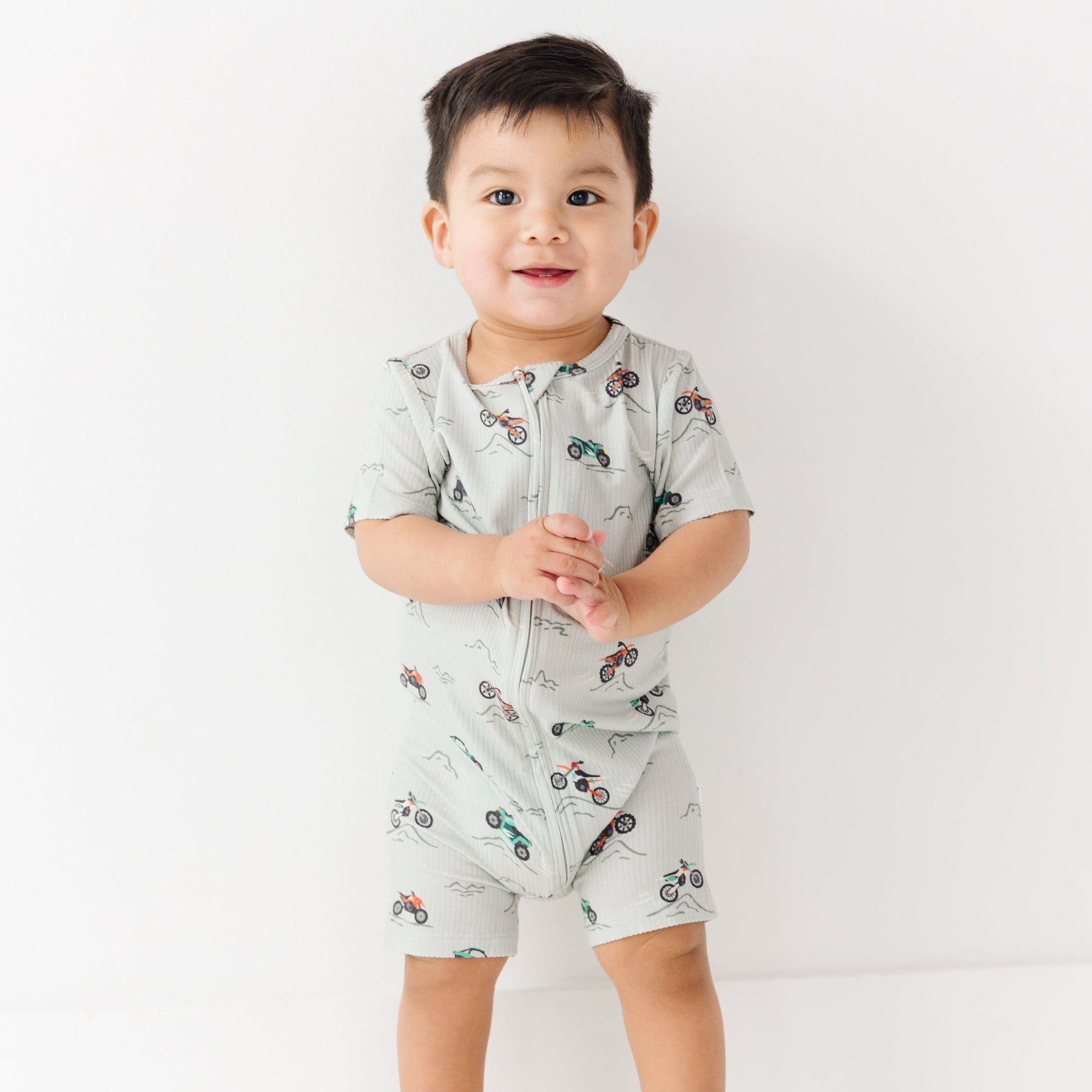 Baby wearing a light gray onesie with vehicle patterns on a white background