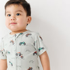 Baby wearing a light gray onesie with vehicle patterns on a white background