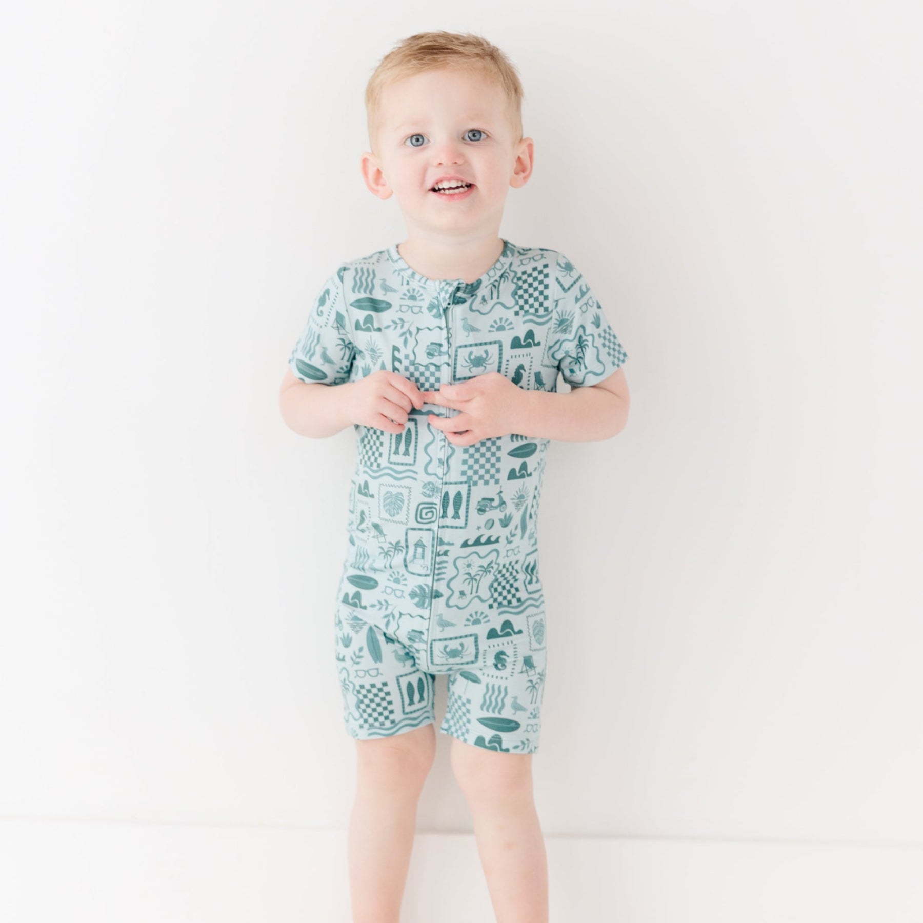 Child wearing a blue short romper with summer patterns on a white background