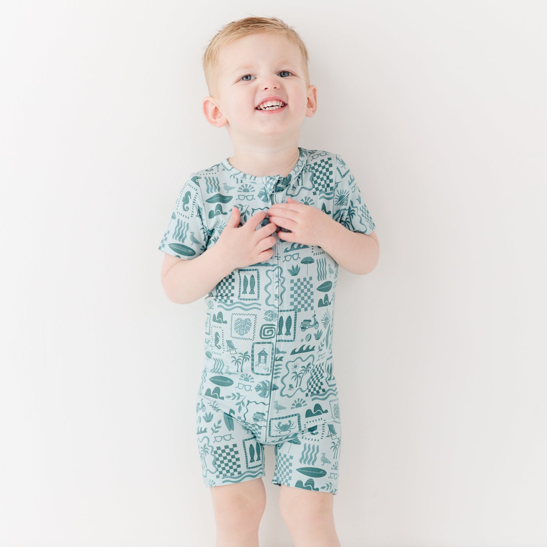 Child wearing a blue short romper with summer patterns on a white background