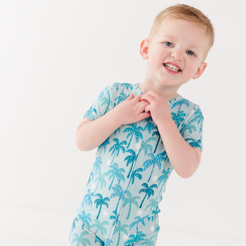 Child wearing a blue palm tree patterned onesie on a white background