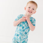 Child wearing a blue palm tree patterned onesie on a white background