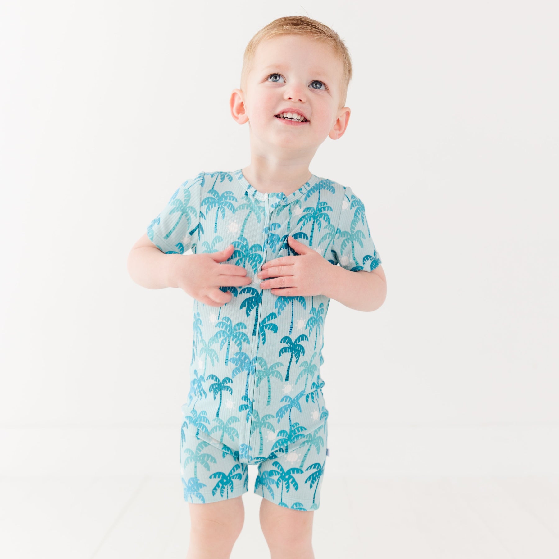 Child wearing a blue palm tree patterned onesie on a white background