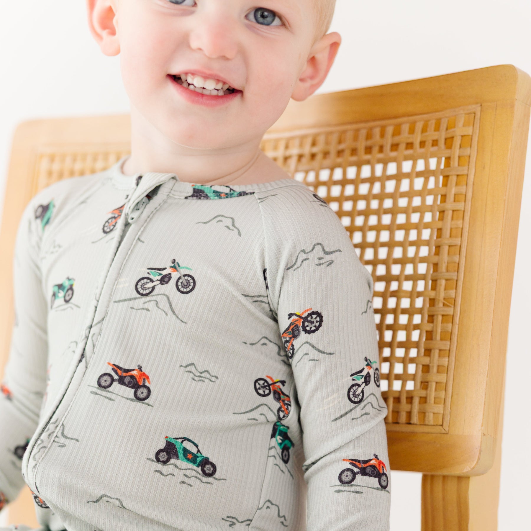 Close up shot of a child wearing a long-sleeve onesie with vehicle patterns on a white background