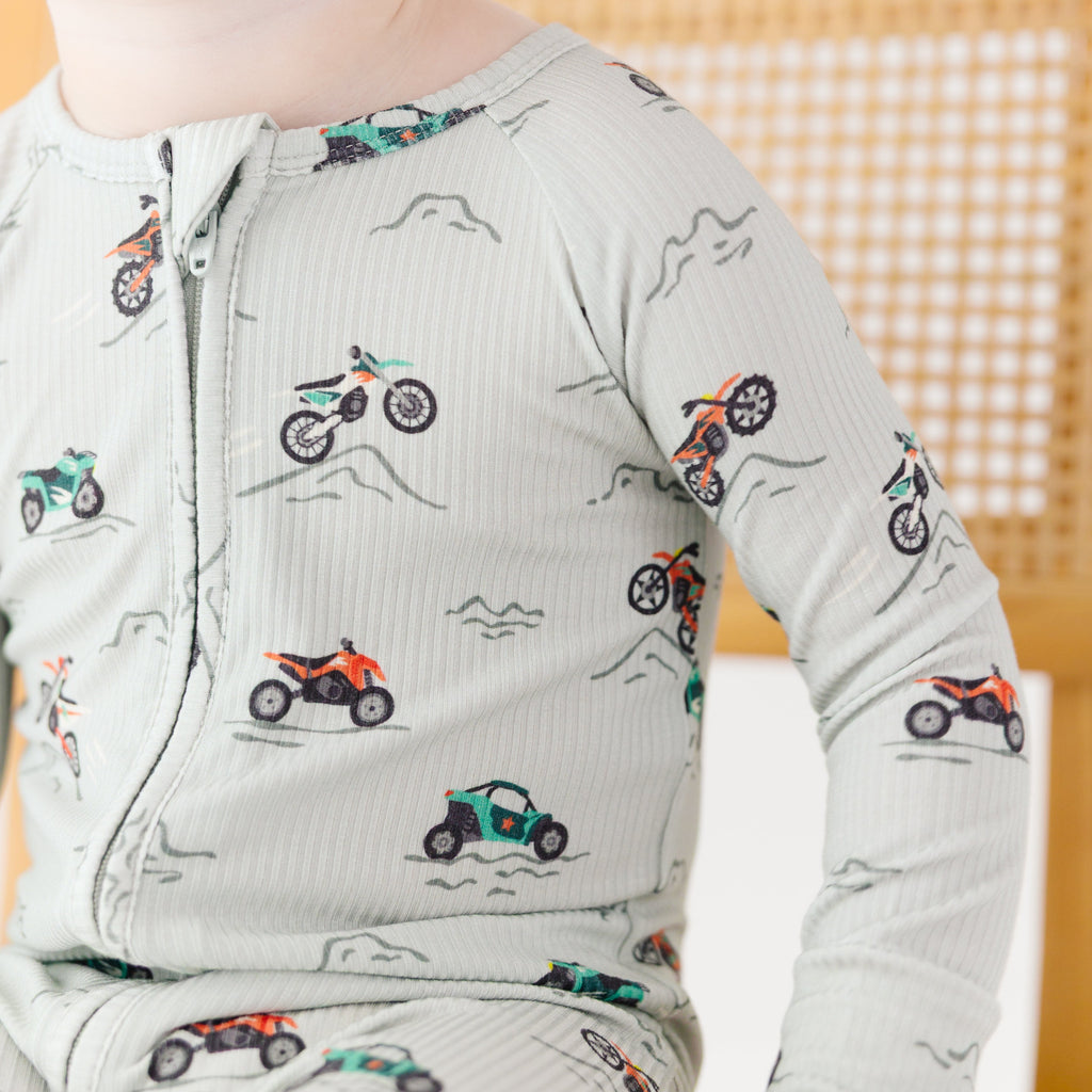 Close up shot of a child wearing a long-sleeve onesie with vehicle patterns on a white background