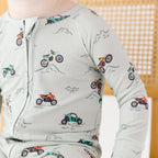 Close up shot of a child wearing a long-sleeve onesie with vehicle patterns on a white background
