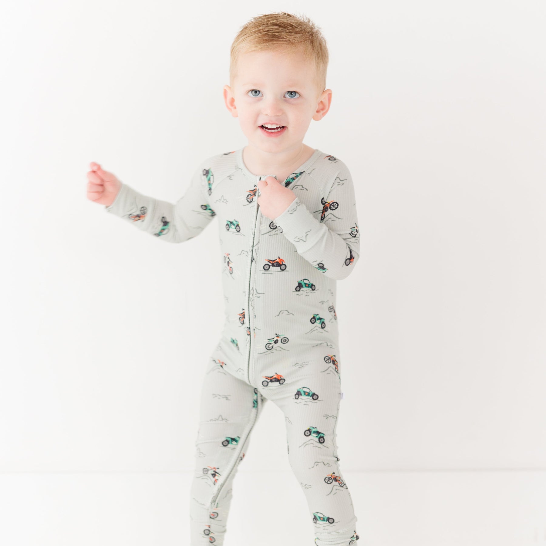 Child wearing a long-sleeve onesie with vehicle patterns on a white background