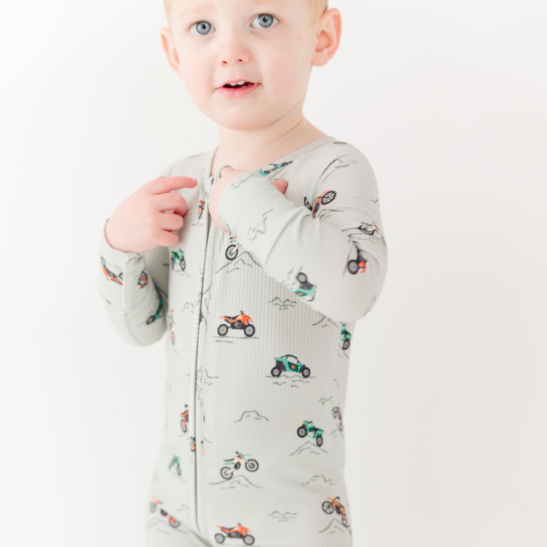 Child wearing a long-sleeve onesie with vehicle patterns on a white background