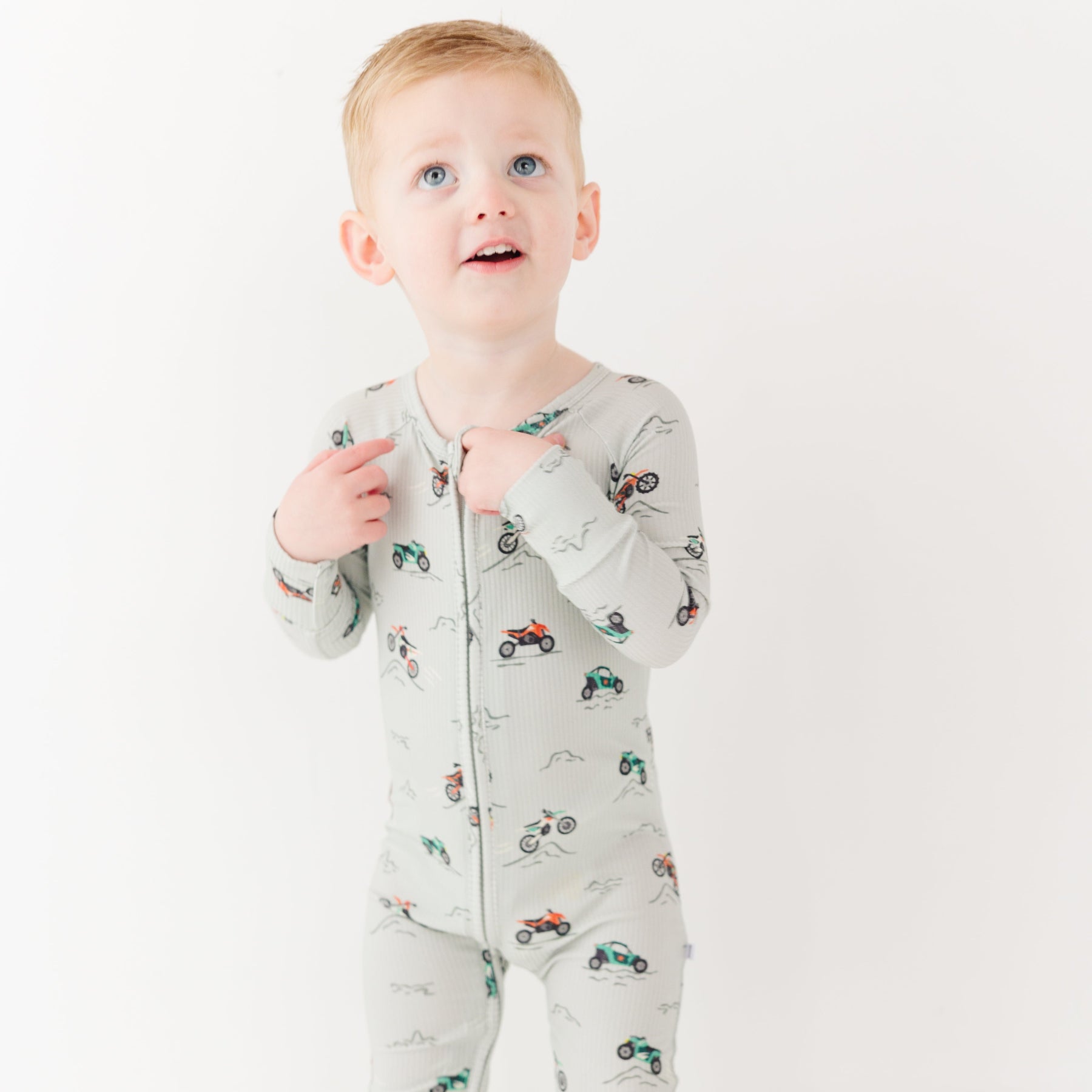 Child wearing a long-sleeve onesie with vehicle patterns on a white background