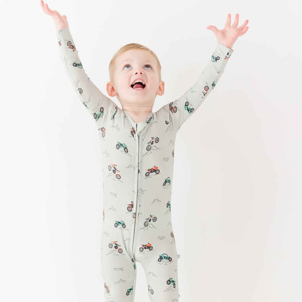 Child wearing a long-sleeve onesie with vehicle patterns on a white background