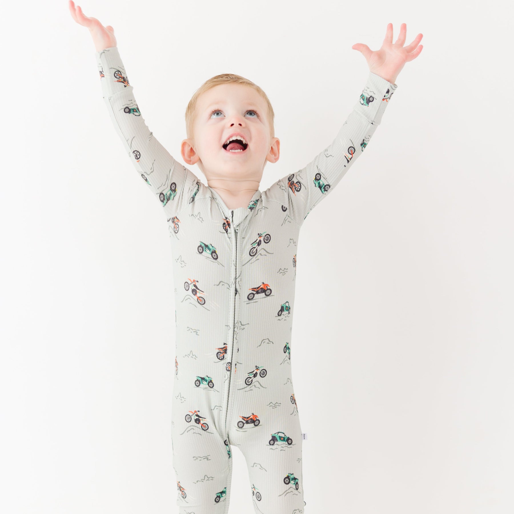 Child wearing a long-sleeve onesie with vehicle patterns on a white background