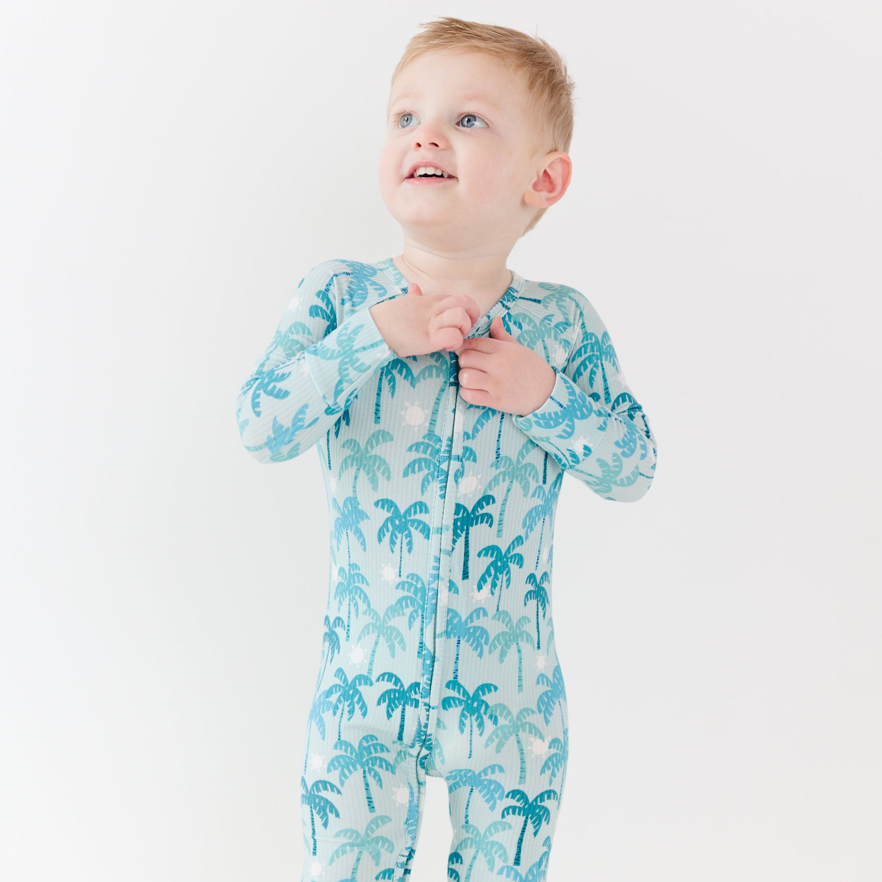 Child wearing a blue palm tree patterned onesie on a white background