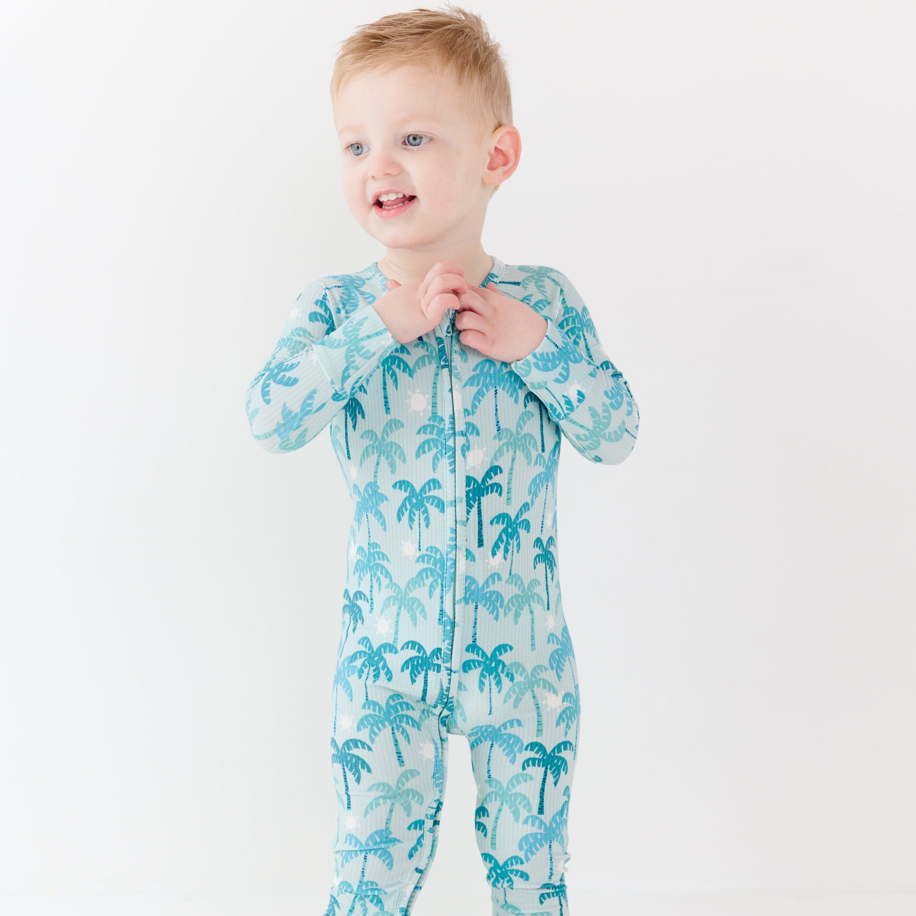 Child wearing a blue palm tree patterned onesie on a white background
