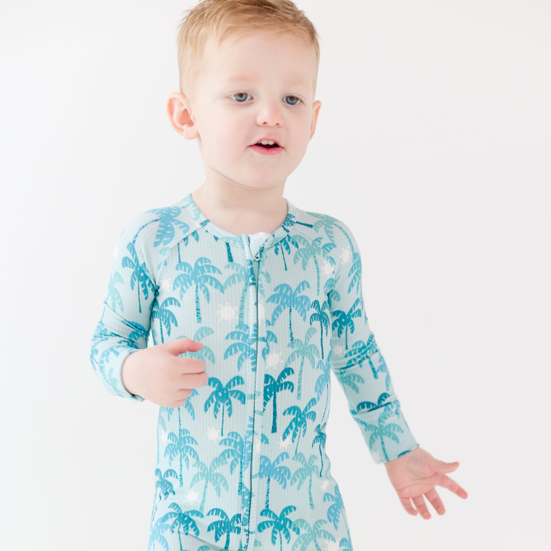 Child wearing a blue palm tree patterned onesie on a white background