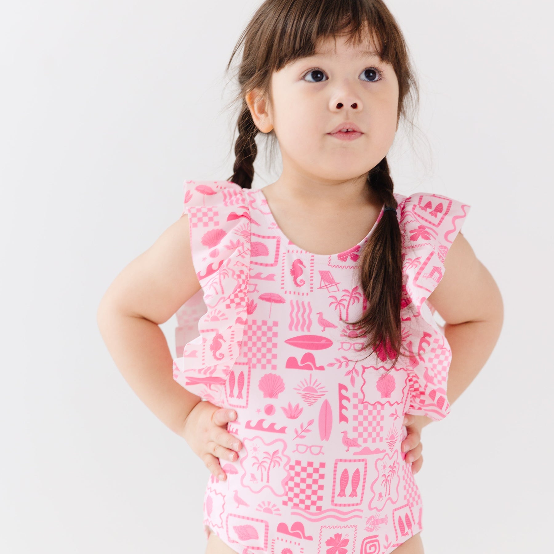 Child wearing a pink and white patterned ruffled one-piece swimsuit on a white background