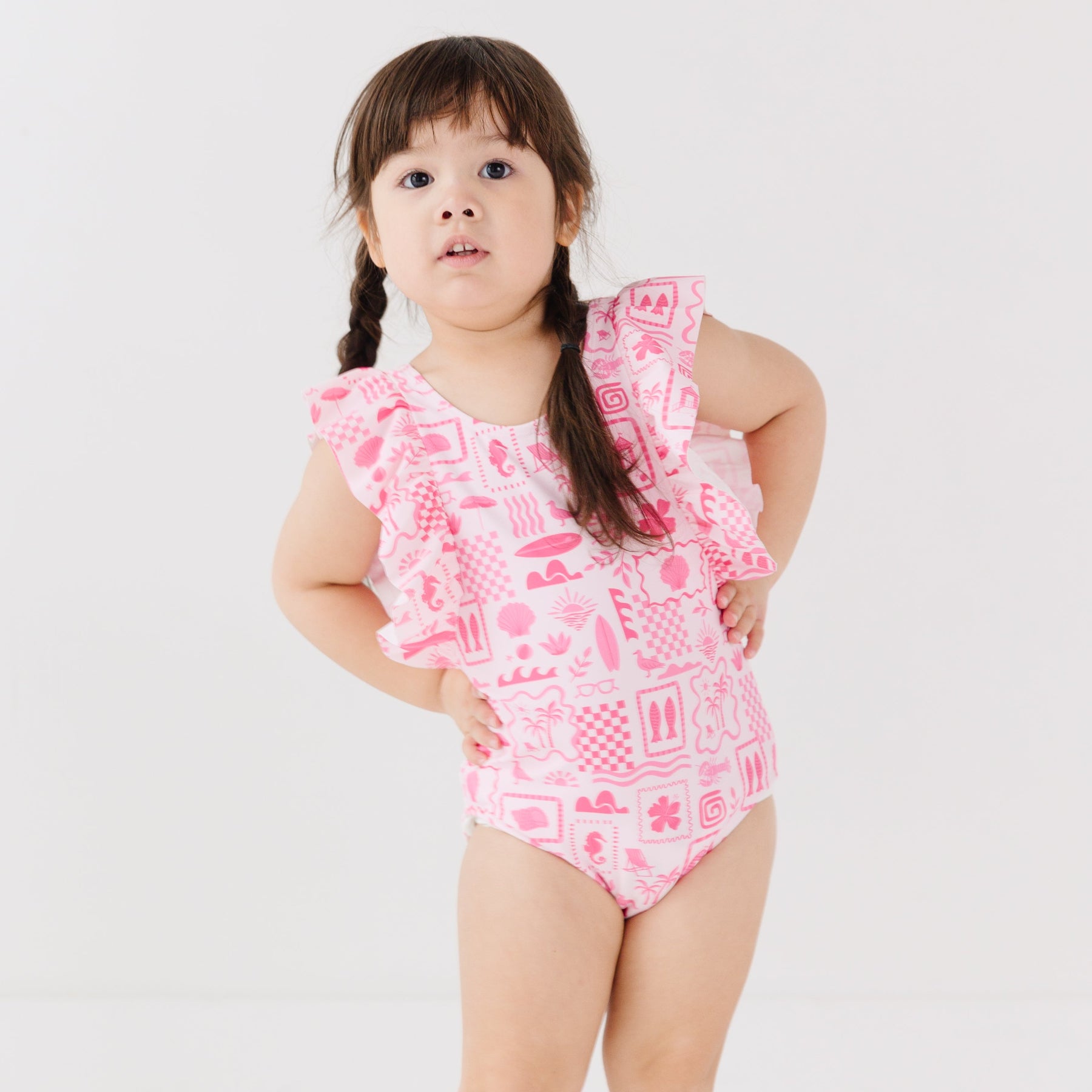 Child wearing a pink and white patterned ruffled one-piece swimsuit on a white background