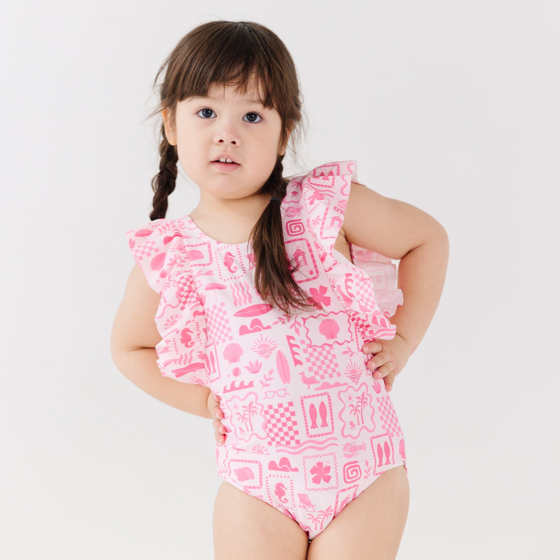 Child wearing a pink and white patterned ruffled one-piece swimsuit on a white background