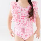 Close up of a child wearing a pink and white patterned ruffled one-piece swimsuit on a white background