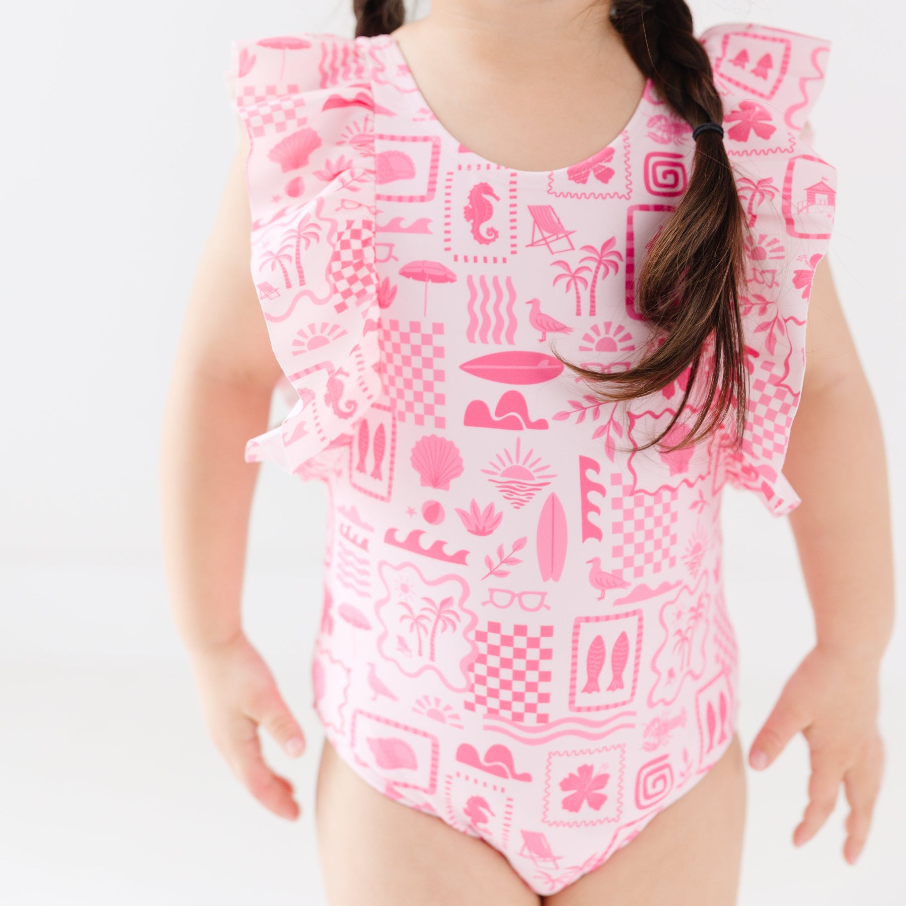 Close up of a child wearing a pink and white patterned ruffled one-piece swimsuit on a white background