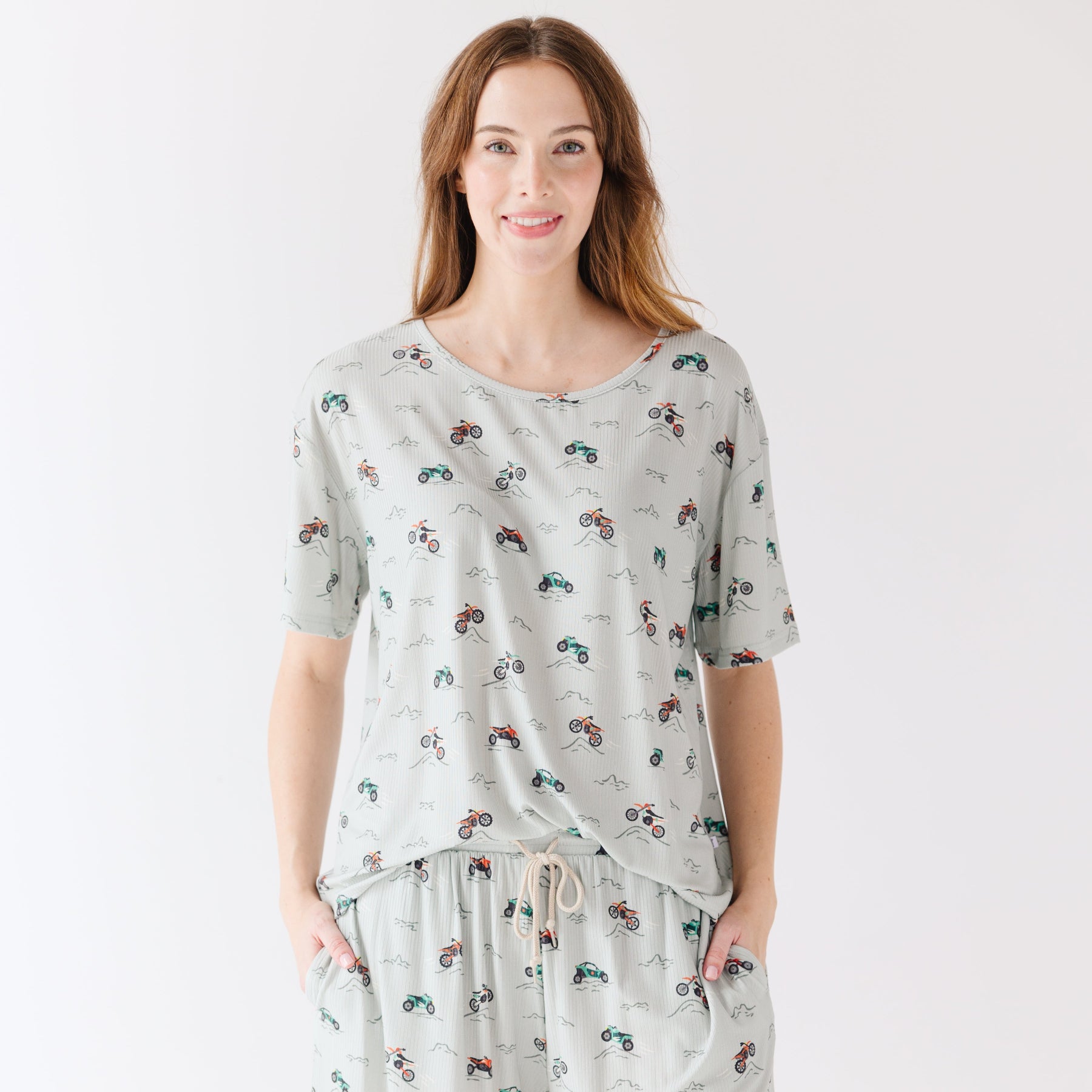 Woman wearing a light gray pajama set with vehicle patterns on a white background