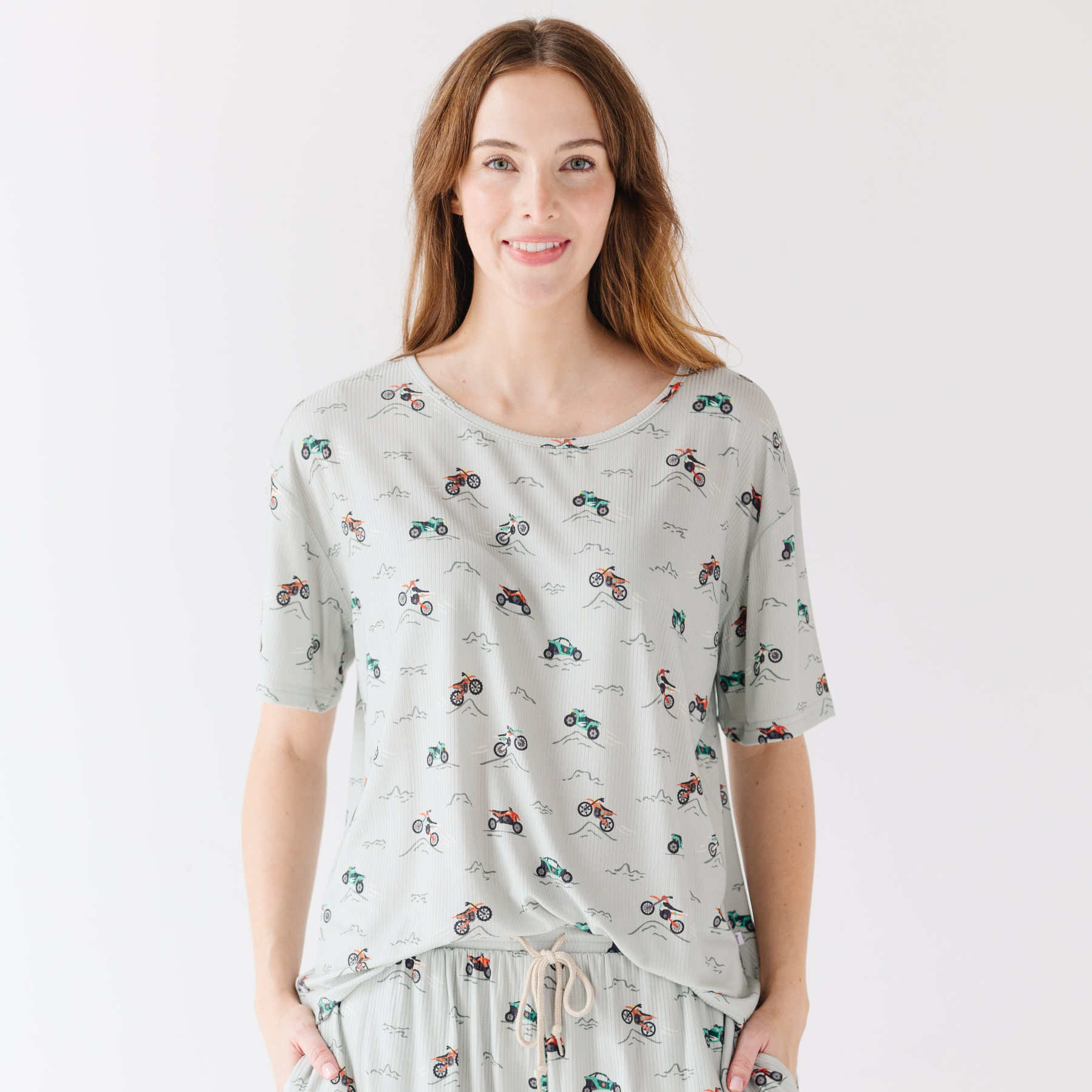 Woman wearing a light gray pajama set with vehicle patterns on a white background
