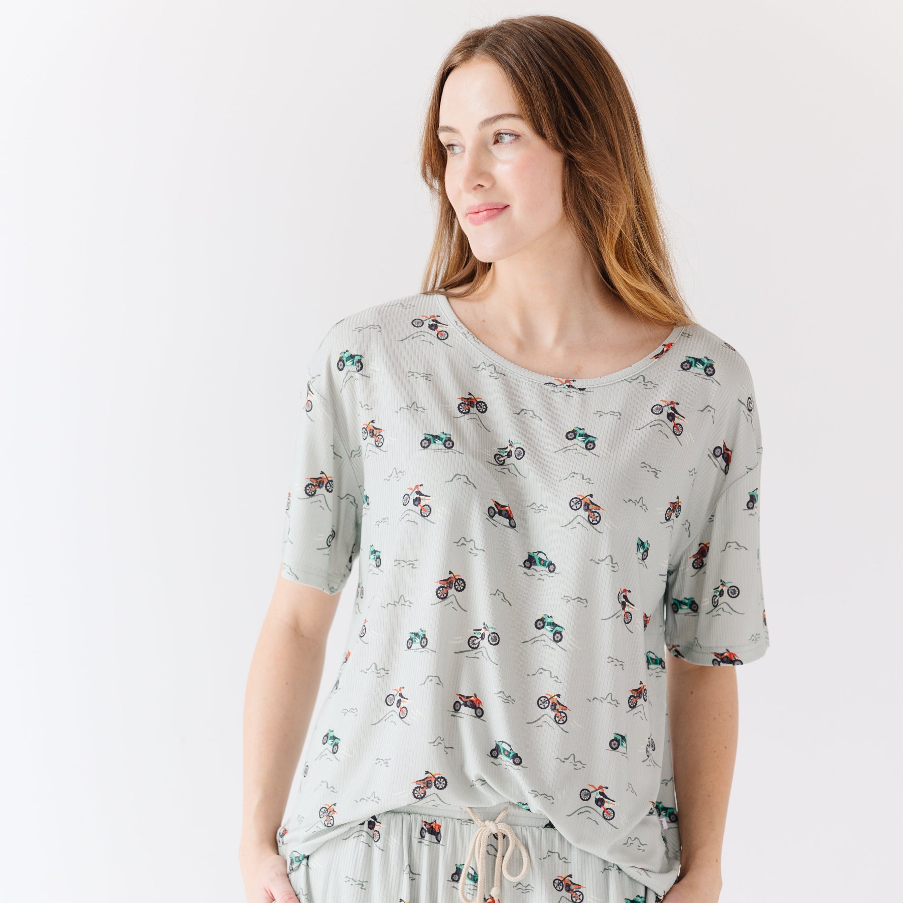 Woman wearing a light gray pajama set with vehicle patterns on a white background