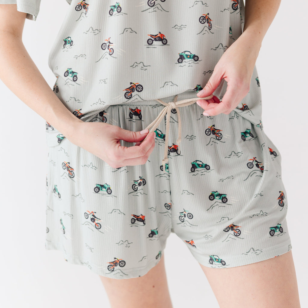Close up shot of a woman wearing a light gray pajama shorts with vehicle patterns on a white background