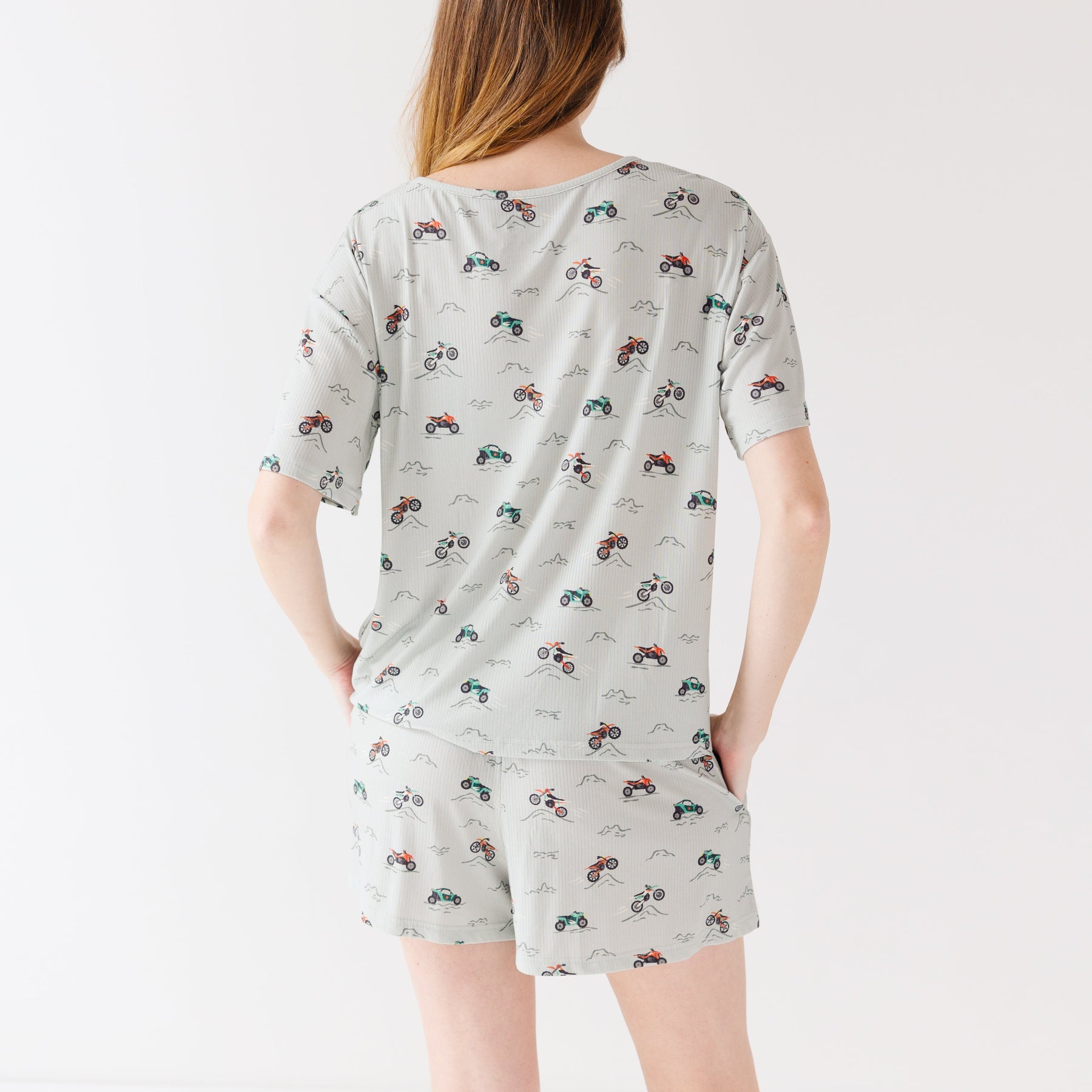 Back view of a woman wearing a light gray pajama set with vehicle patterns on a white background