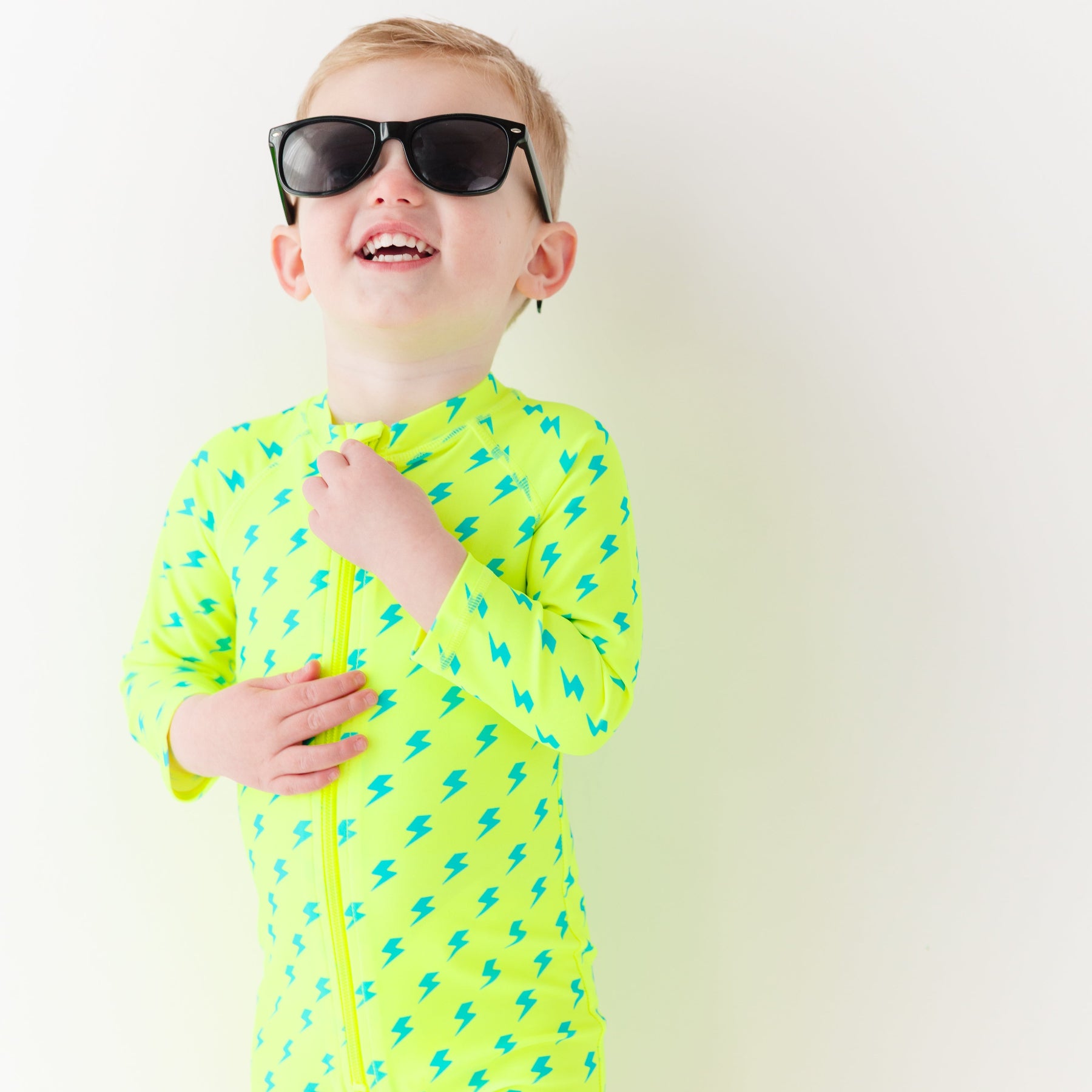 Child wearing a bright yellow boy swimsuit with a lightning bolt pattern and sunglasses on a white background