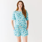 Woman wearing a blue palm tree patterned pajama set on a white background