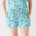 Woman wearing a blue palm tree patterned pajama shorts on a white background