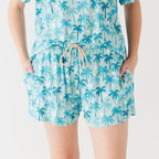 Woman wearing a blue palm tree patterned pajama shorts on a white background