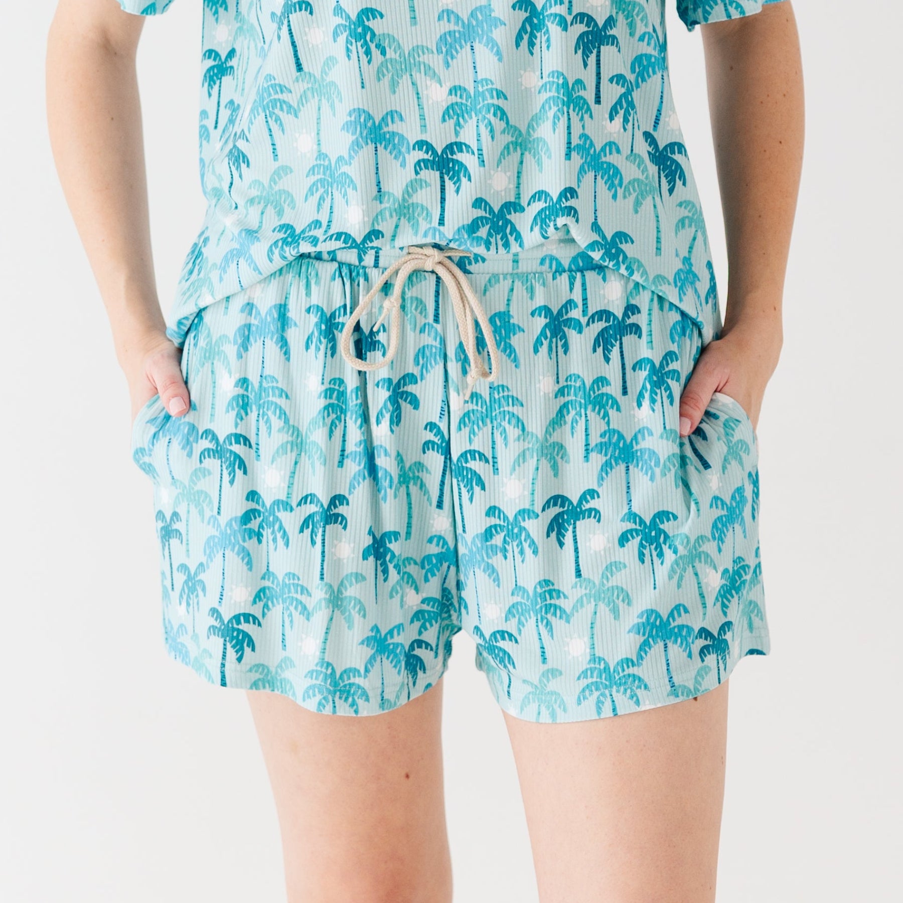 Woman wearing a blue palm tree patterned pajama shorts on a white background