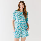 Woman wearing a blue palm tree patterned pajama set on a white background