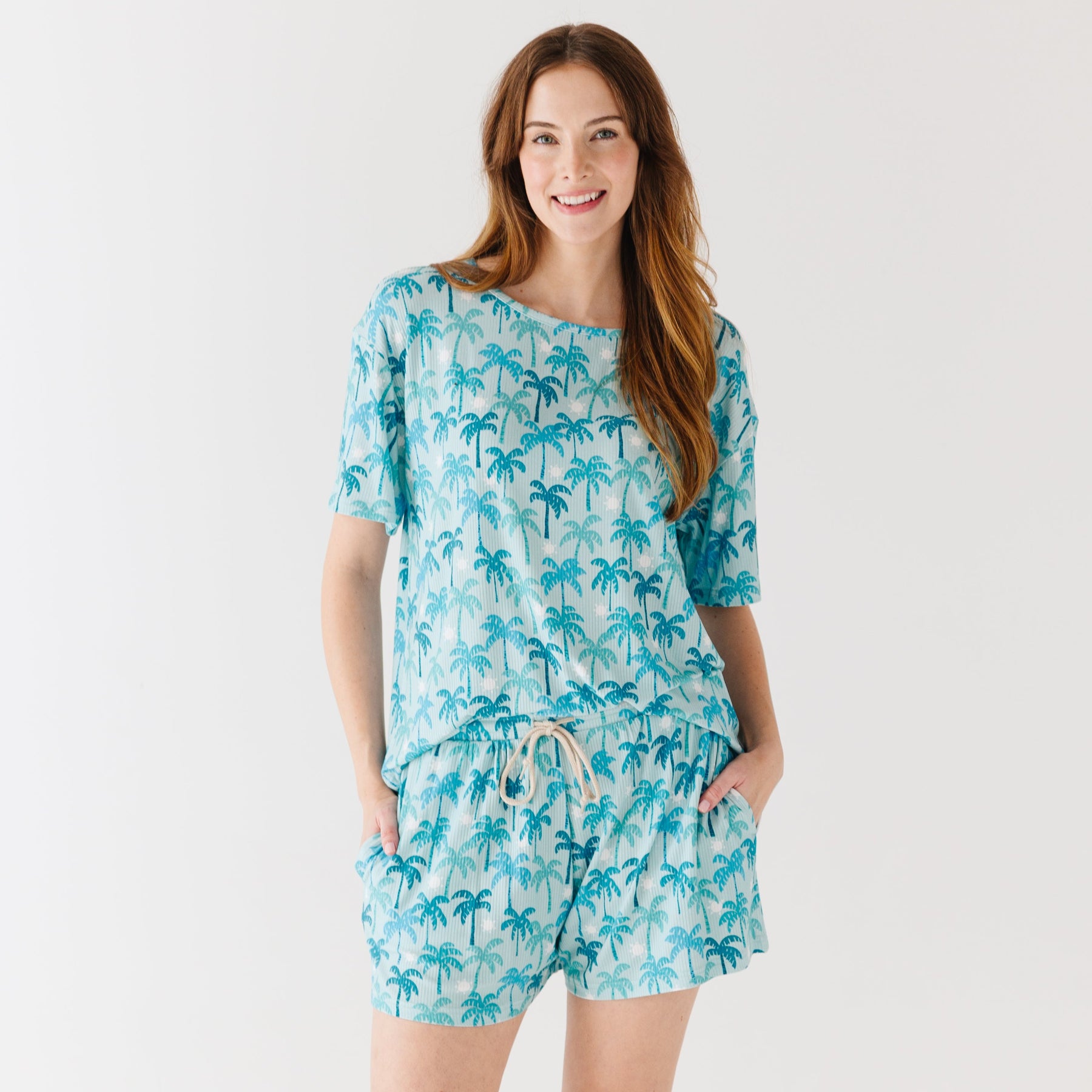 Woman wearing a blue palm tree patterned pajama set on a white background