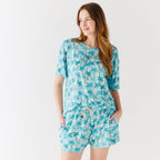 Woman wearing a blue palm tree patterned pajama set on a white background