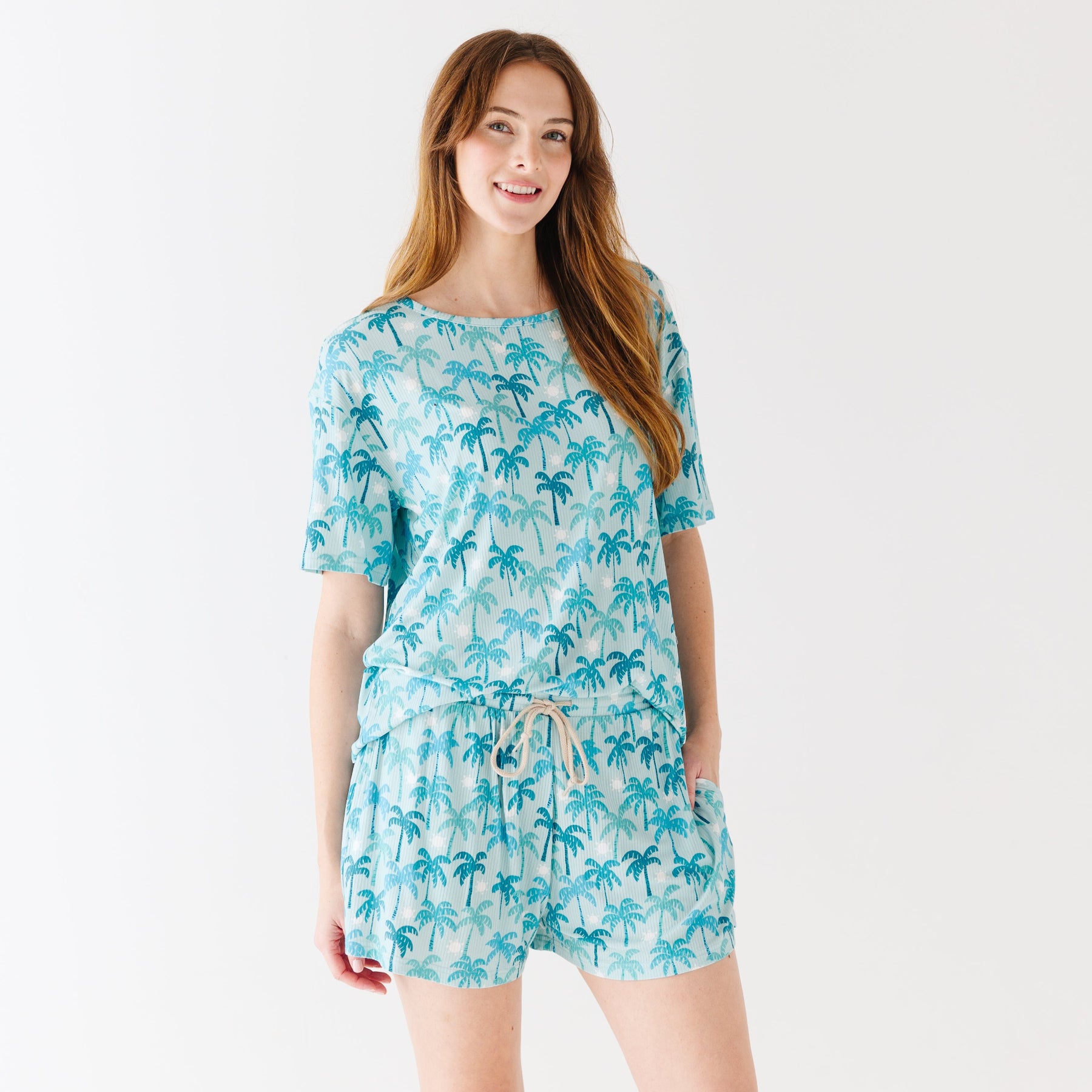 Woman wearing a blue palm tree patterned pajama set on a white background