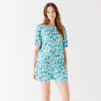 Woman wearing a blue palm tree patterned pajama set on a white background