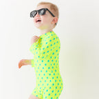 Child wearing a bright yellow boy swimsuit with a lightning bolt pattern and sunglasses on a white background