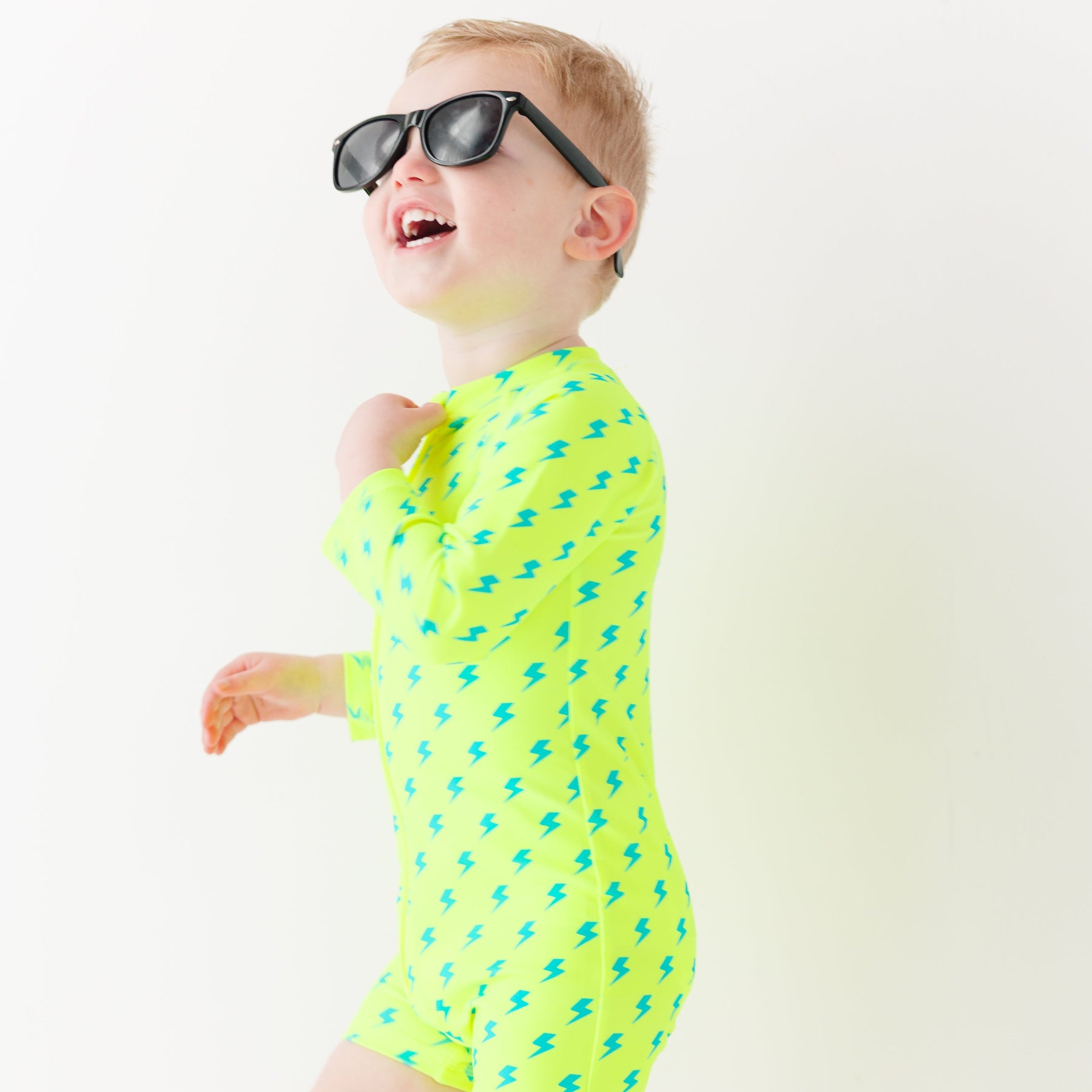 Child wearing a bright yellow boy swimsuit with a lightning bolt pattern and sunglasses on a white background
