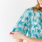 Close up shot of a woman wearing a blue palm tree patterned pajama on a white background