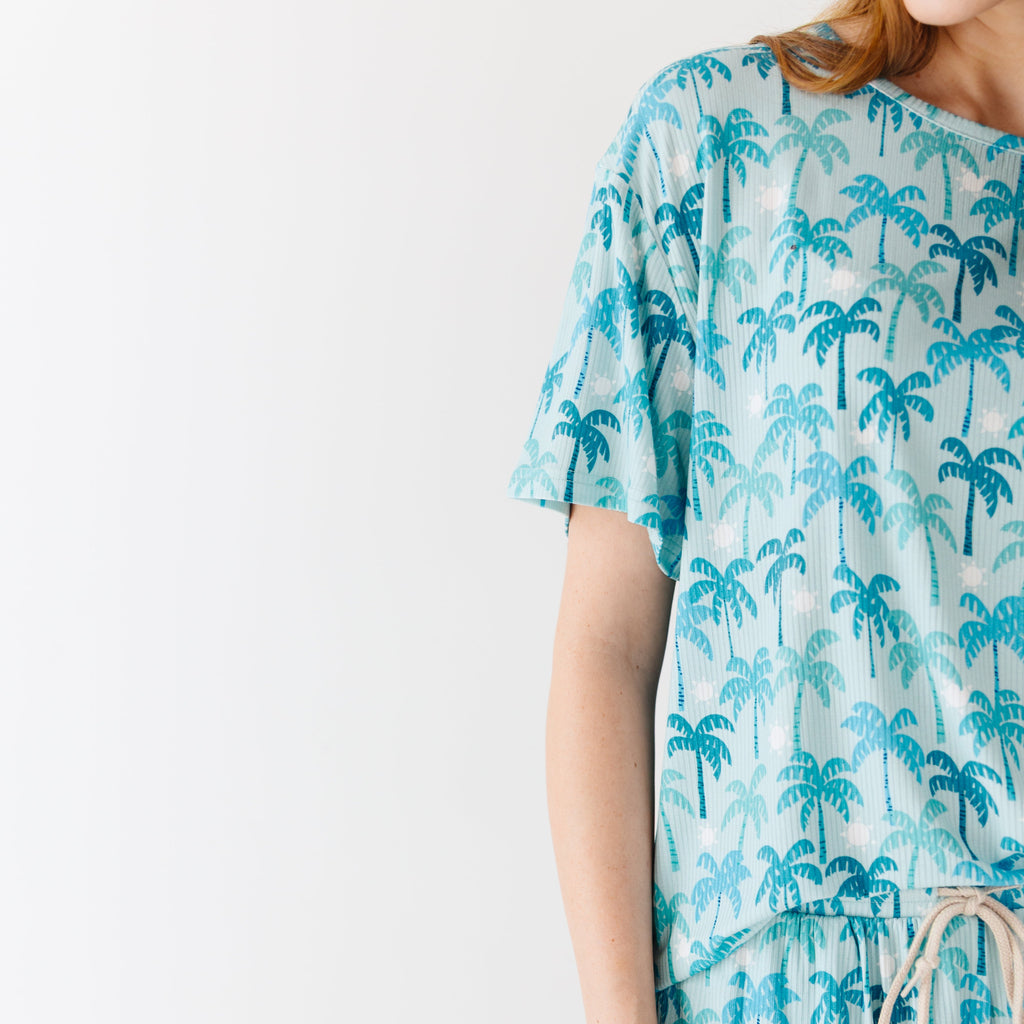 Close up shot of a woman wearing a blue palm tree patterned pajama on a white background