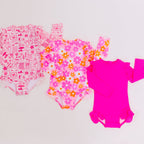 Three pink baby one-piece swimsuits with different patterns on a white background
