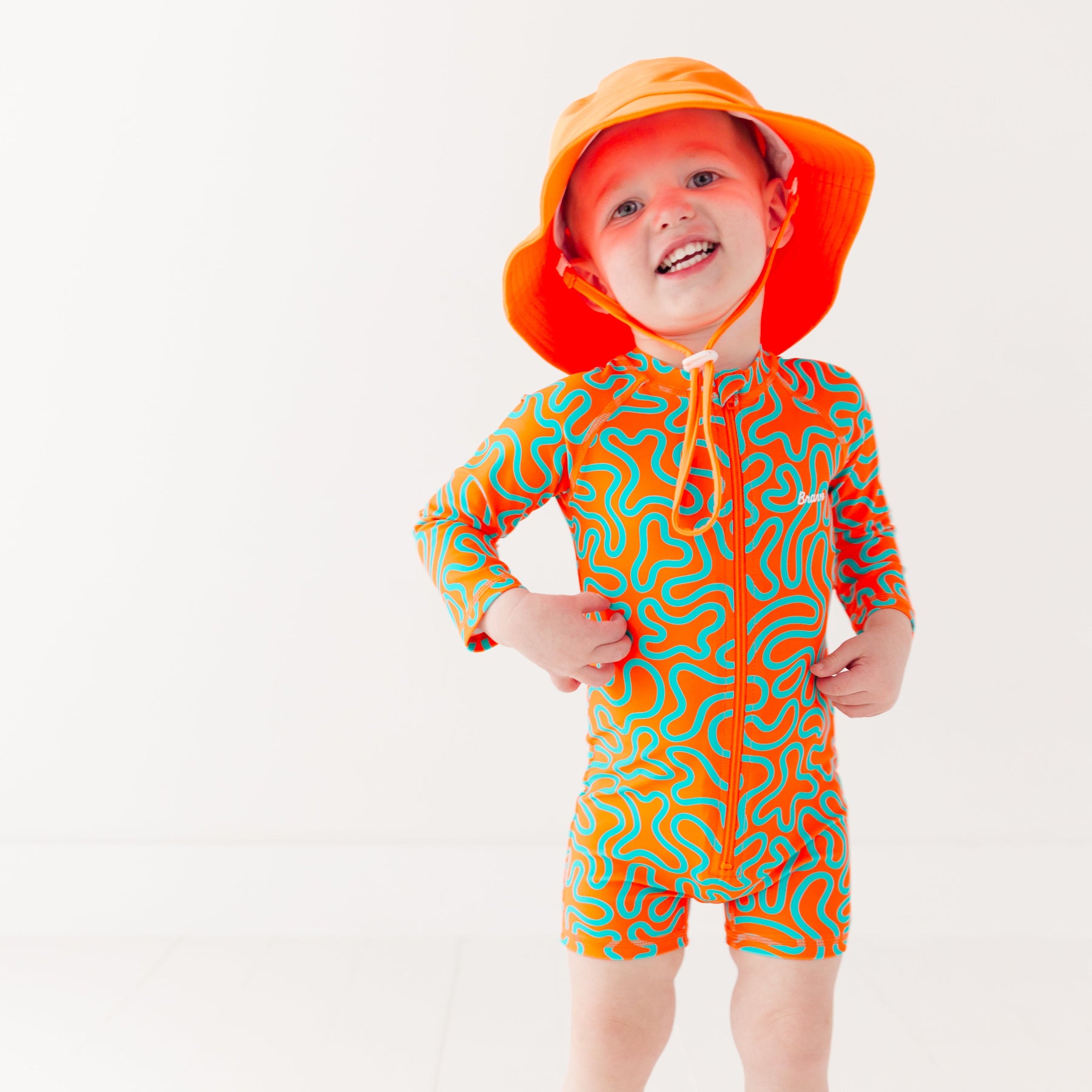 Child wearing a colorful swimsuit with a squiggly pattern and an orange bucket hat on a white background