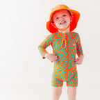 Child wearing a colorful swimsuit with a squiggly pattern and an orange bucket hat on a white background