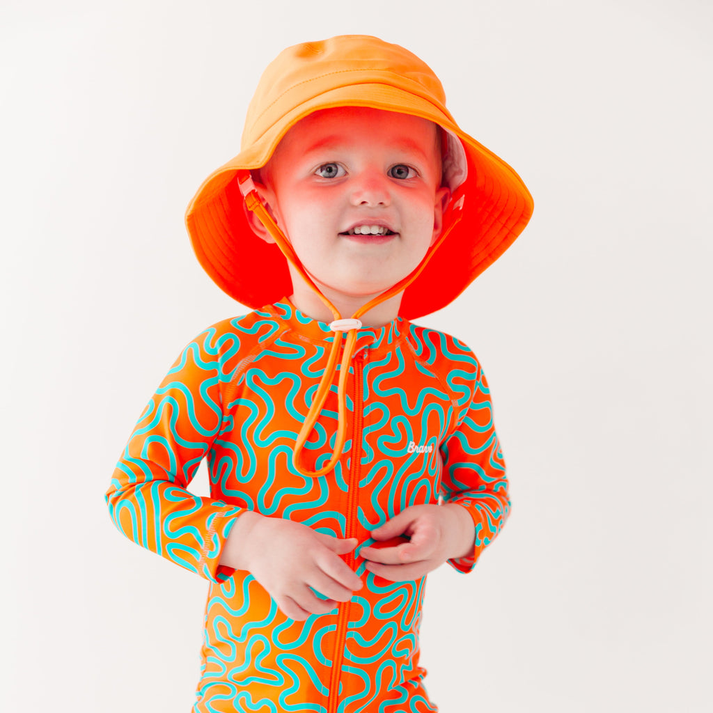 Child wearing a colorful swimsuit with a squiggly pattern and an orange bucket hat on a white background