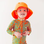 Child wearing a colorful swimsuit with a squiggly pattern and an orange bucket hat on a white background