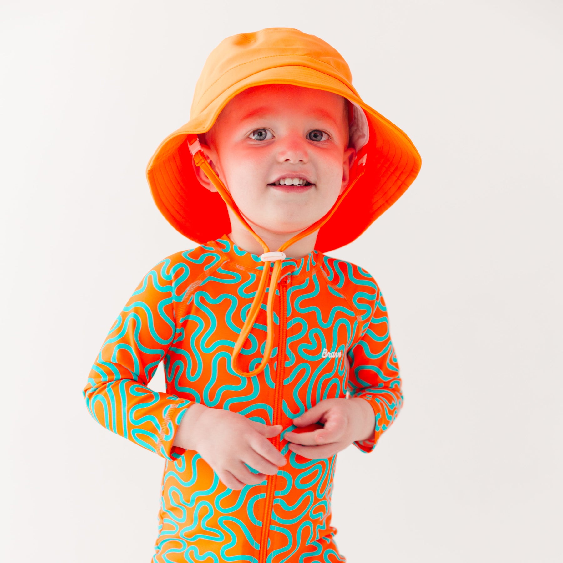 Child wearing a colorful swimsuit with a squiggly pattern and an orange bucket hat on a white background