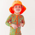Child wearing a colorful swimsuit with a squiggly pattern and an orange bucket hat on a white background
